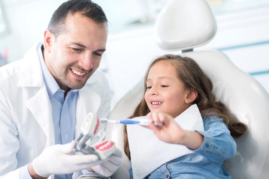 dentist shows young patient how to brush teeth